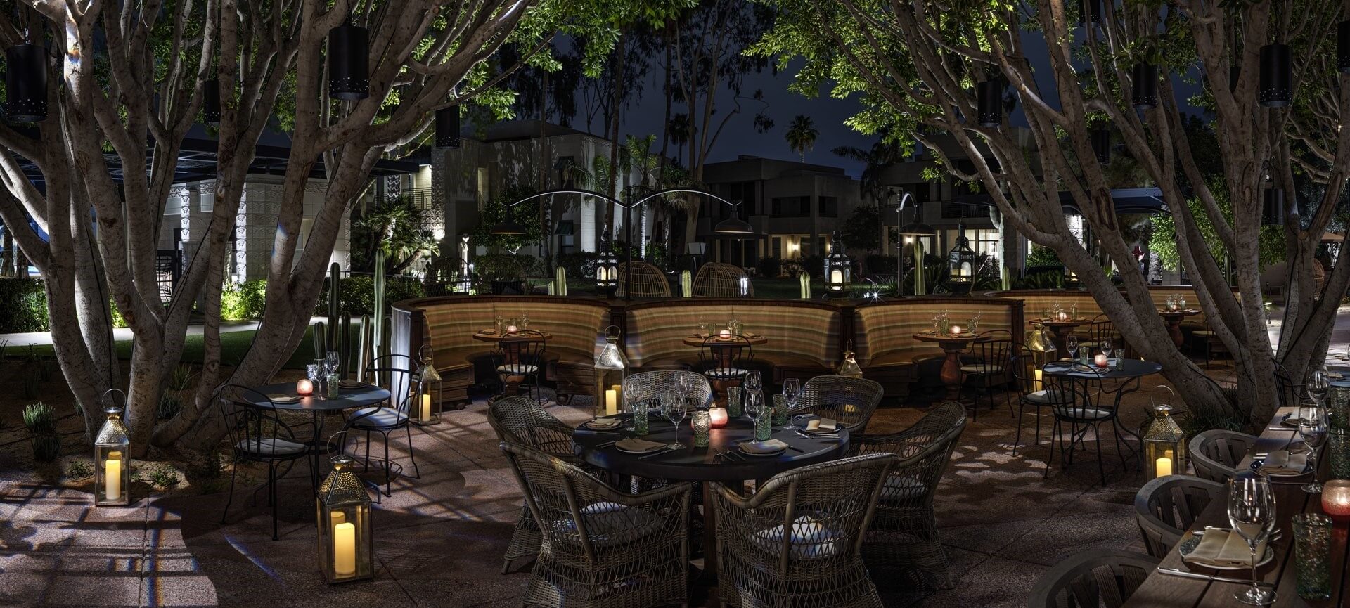 An open-air restaurant patio at night features wicker chairs and tables set with plates, glasses, and condiments. Surrounded by trees and lit by candle lanterns, it offers a cozy atmosphere akin to a paradise garden. In the background, modern buildings are partially visible.
